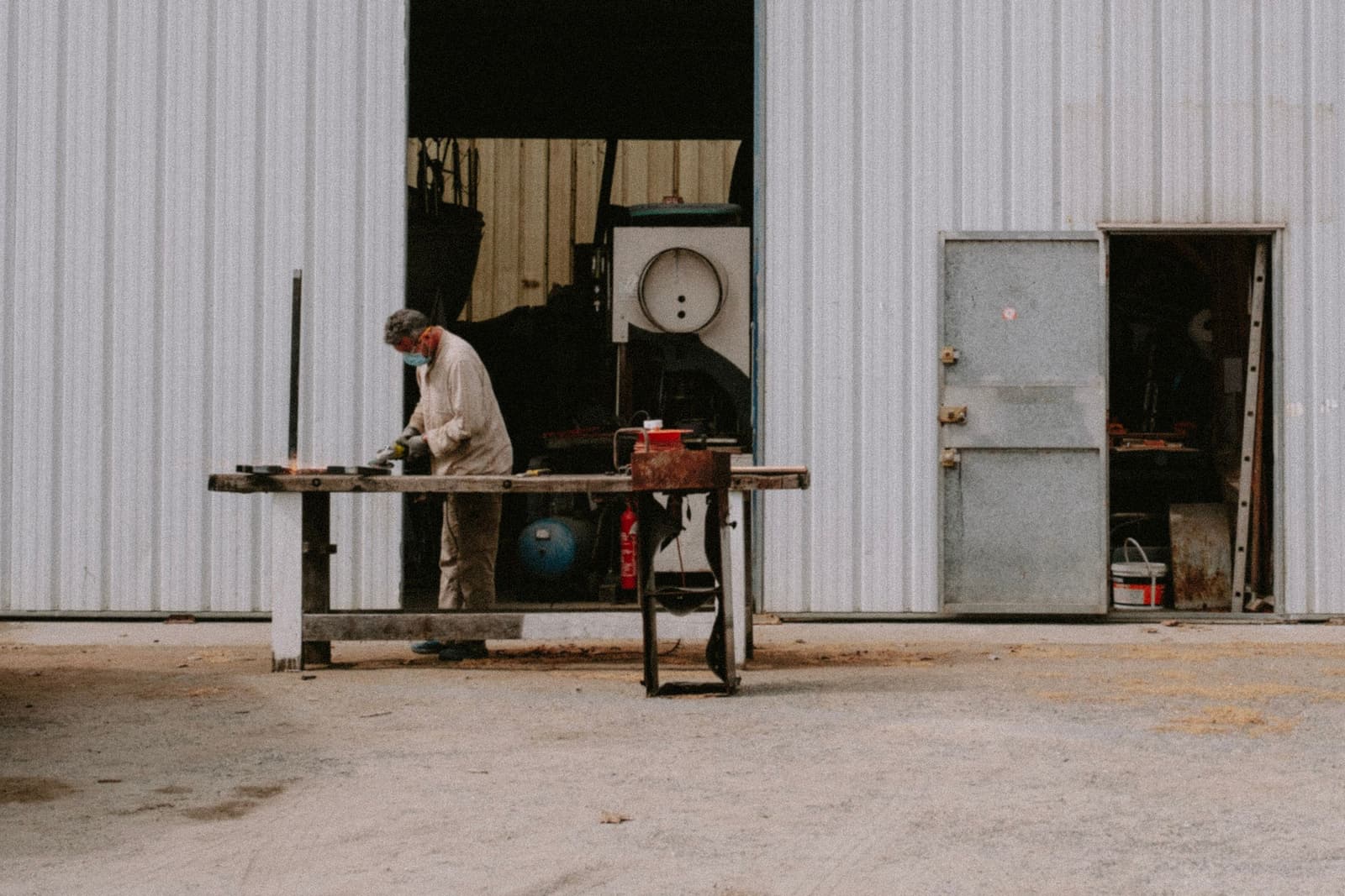 A technician grinding a part at a bench outside the shop's open bay door